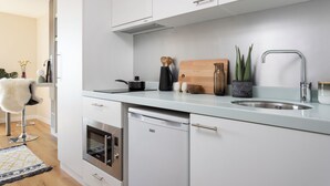 Una cucina moderna con mobili bianchi, un lavello in acciaio inossidabile, un tagliere di legno e una macchina da caffè.