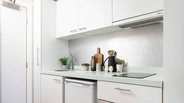 Una cucina moderna con mobili bianchi, lavastoviglie, forno integrato e un piano di lavoro con diversi oggetti da cucina.