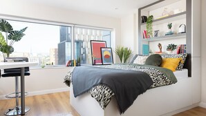 Una camera da letto moderna con un'ampia finestra, un letto con biancheria a motivi, una scrivania con sedia e una libreria con diversi oggetti.