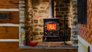 A stone fireplace with a wood-burning stove, a red cloth on the floor, and a wooden wall with plaques. - 1 Bed in Crook (oc-78487) (North Bitchburn)
