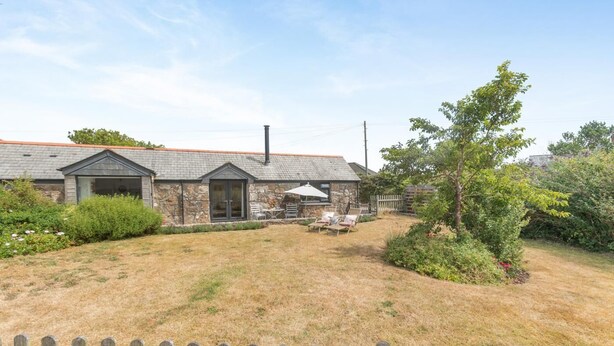 Ein Steinhaus mit umzäuntem Garten, einer Terrasse mit Stühlen und einem Baum.