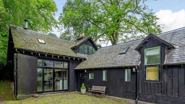 A rustic wooden building with a large glass door entrance, a bench, and a small garden area. - 2 Bed in Inverness (oc-78537) (Drumnadrochit)