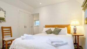 A neatly made bed with pillows, a bedside lamp, a chair, and a wardrobe in a well-lit room. - 2 Bed in Inverness (oc-78537) (Drumnadrochit)