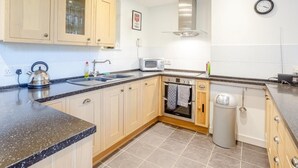 A modern kitchen with wooden cabinets, a stainless steel kettle, a microwave, and a built-in oven. - 2 Bed in Inverness (oc-78537) (Drumnadrochit)