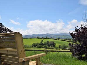 A wooden bench overlooking a green field with a mountain range in the distance. - 2 Bed in Llanwrst (oc-78601) (Llanddoged)