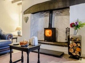 A cozy living room with a stone fireplace, a blue sofa, a table with a lamp, and a vase with flowers. - 2 Bed in Llanwrst (oc-78601) (Llanddoged)