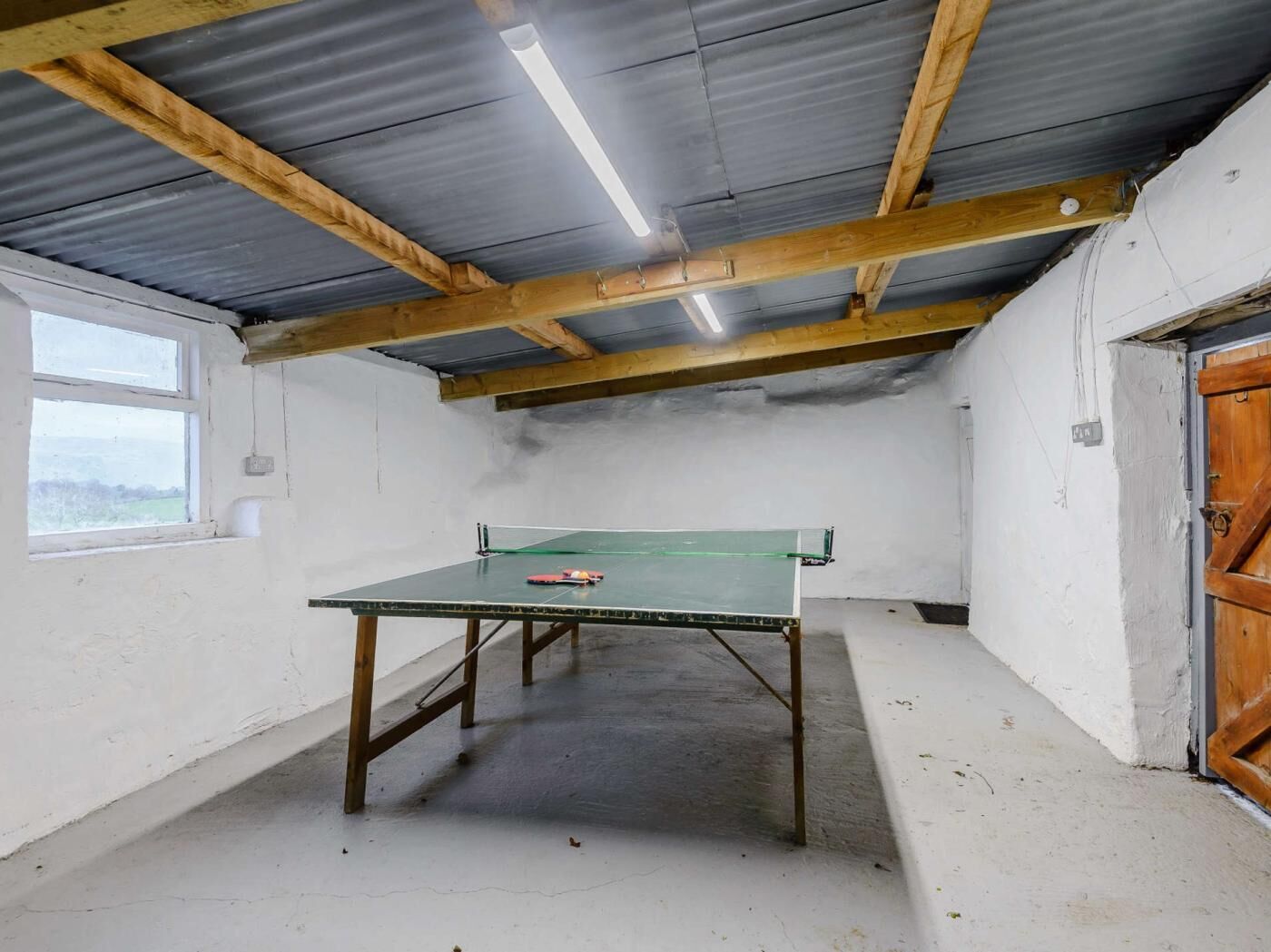 Ein Tischtennis-Tisch in einem Raum mit hoher Decke, Holzbalken, einem Fenster und einer Tür.