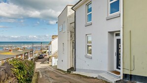 En gata längs kusten med vita byggnader, en klar himmel och utsikt över havet.