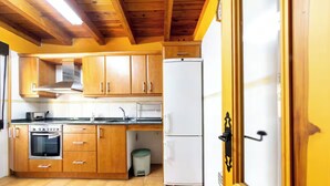 A kitchen with wooden cabinets, a white refrigerator, a stove, and a trash bin. - ANCLA Country House: Ideal for families, with a barbecue, outdoor space, and a game room (Barca)