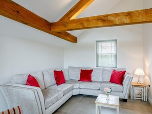 A living room with a grey sectional sofa, red cushions, a small white table with a vase, and a lamp on a side table. - 5 Bed in Market Rasen (oc-78678) (Tealby)