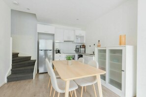 A modern kitchen with white cabinetry, a stainless steel refrigerator, and a dining area with a wooden table and chairs. - Beautiful 3BDR 2BA Townhouse in St Kilda East (Saint Kilda East)