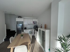 A compact kitchen with white cabinets, a refrigerator, a coffee maker, and a dining area with a table and chairs. - Beautiful 3BDR 2BA Townhouse in St Kilda East (Saint Kilda East)