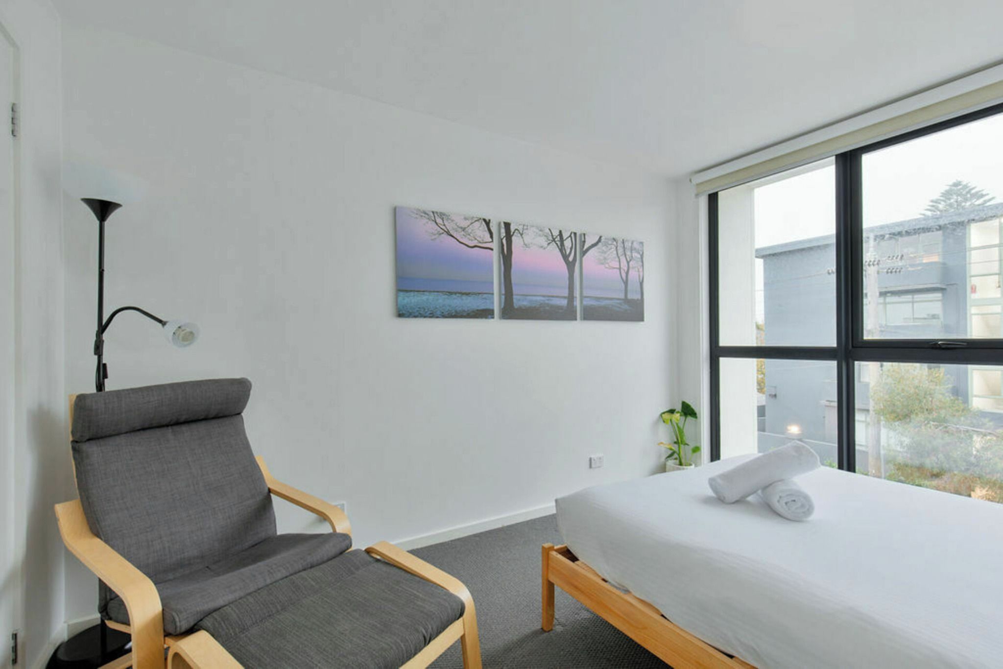 A hotel room with a bed, a chair, a window, and artwork on the wall.
