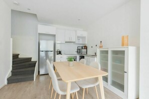 Eine moderne Küche mit weißen Schränken, einem Edelstahlkühlschrank und einem Essbereich mit einem Holztisch und Stühlen.