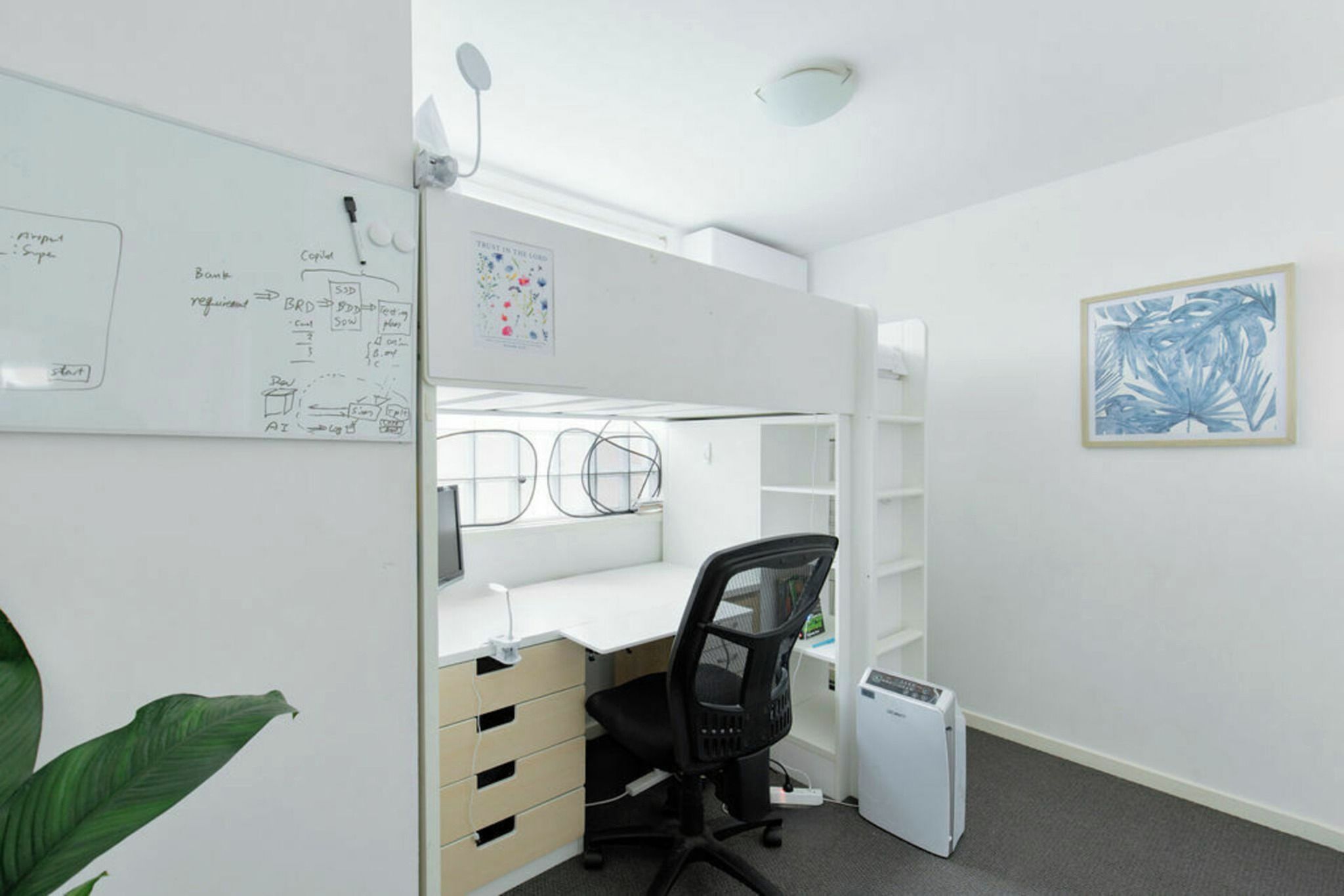 Ein kompakter Arbeitsbereich mit einer Whiteboardwand, einem Schreibtisch, einem Stuhl, einem kleinen Drucker und einer Pflanze.