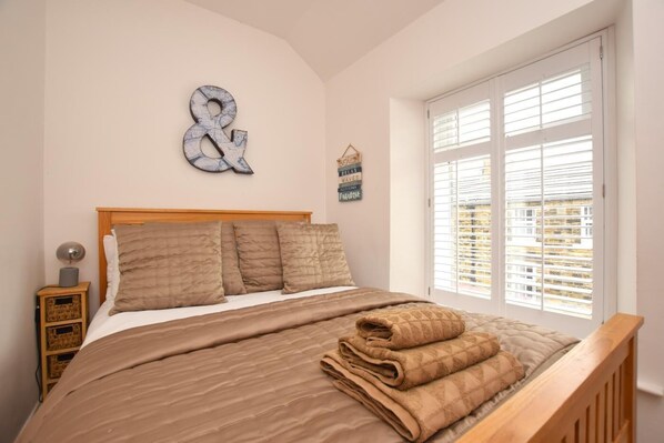 A bedroom with a bed, a wooden headboard, a window with blinds, a bedside table with a lamp, and a wall decoration.