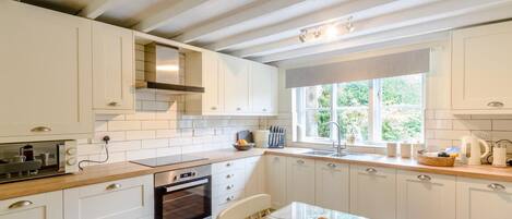 Una cocina con armarios blancos, una estufa, un horno, una ventana y una mesa con sillas.