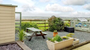Een terras met een houten tafel en bankjes, omringd door plantenbakken en uitzicht op het landschap.