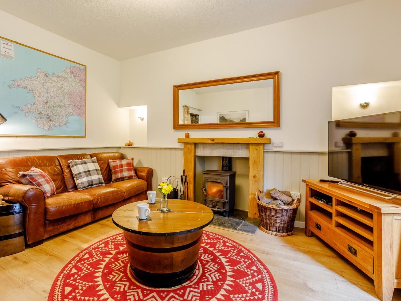 A cozy living room with a leather sofa, a round wooden coffee table, a fireplace, a television, and a map on the wall.