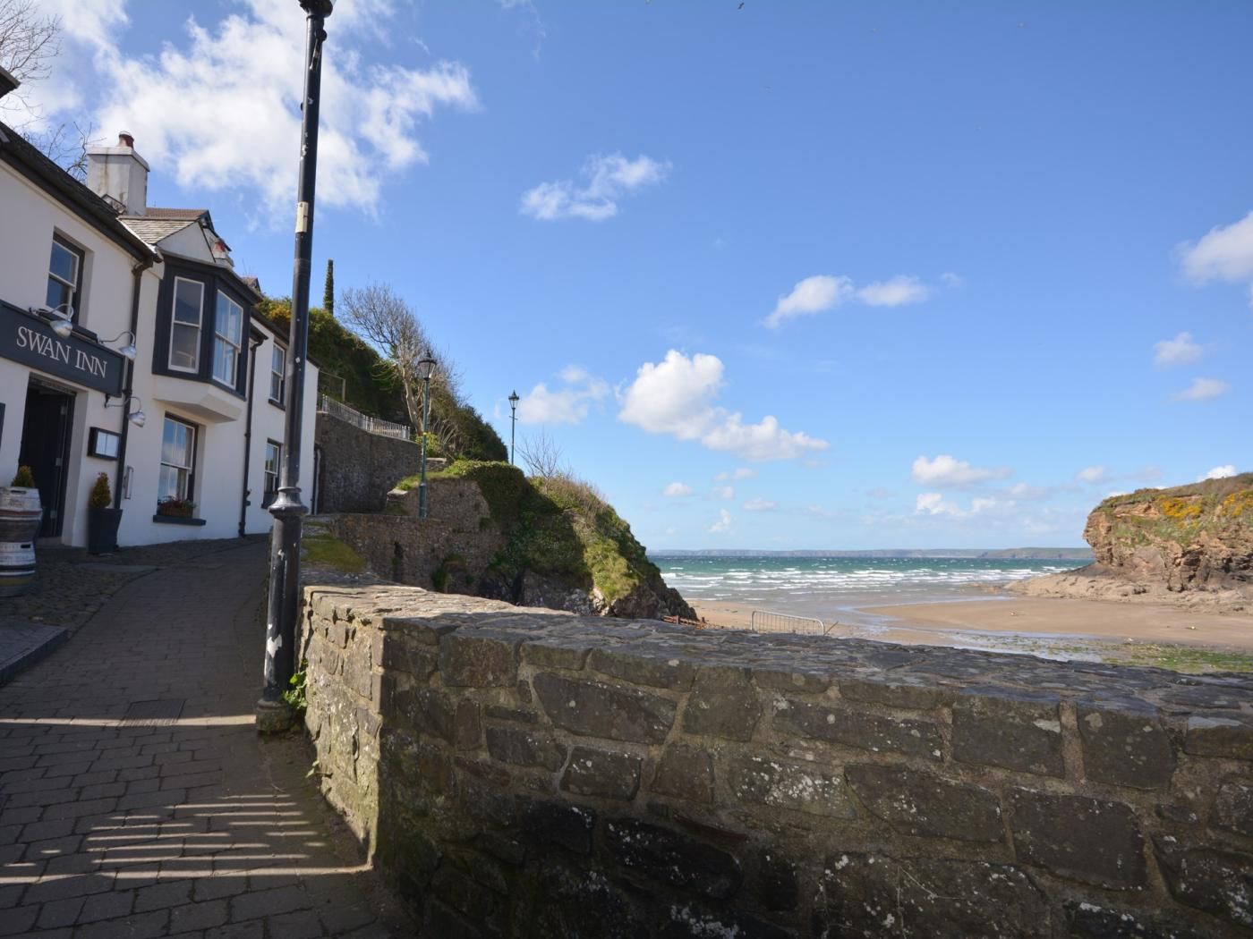 A coastal building named 'Swan Inn' with a stone wall and a paved walkway leading to the beach.
