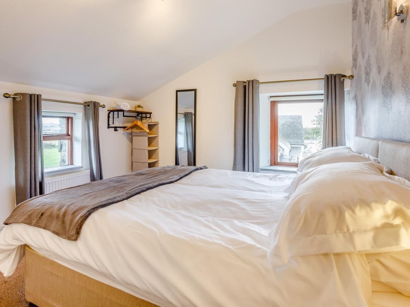 A bedroom with a bed, a window, a mirror, and a view of the outside.