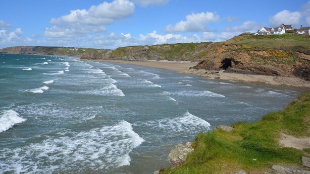 Een kustlandschap met een strand, rotsachtige kliffen en een huis op de helling.