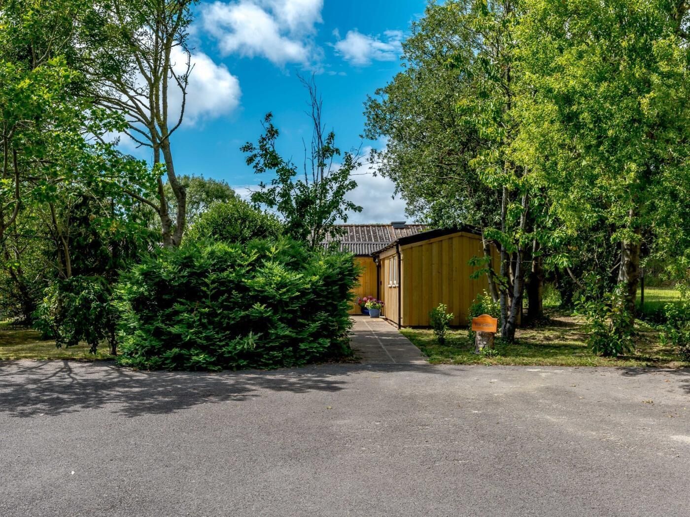 Een laag gebouw met een schuin dak, omgeven door weelderige begroeiing en bomen.