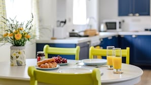 A breakfast setup with a table, chairs, a vase of flowers, croissants, grapes, and a glass of orange juice.