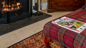 Una habitación acogedora con chimenea, un sofá de cuadros y un aparador de madera.