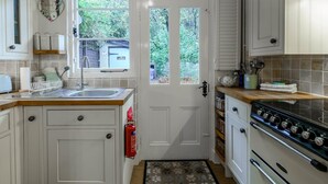 Una cocina con armarios blancos, estufa, fregadero y ventana con vistas a la vegetación.