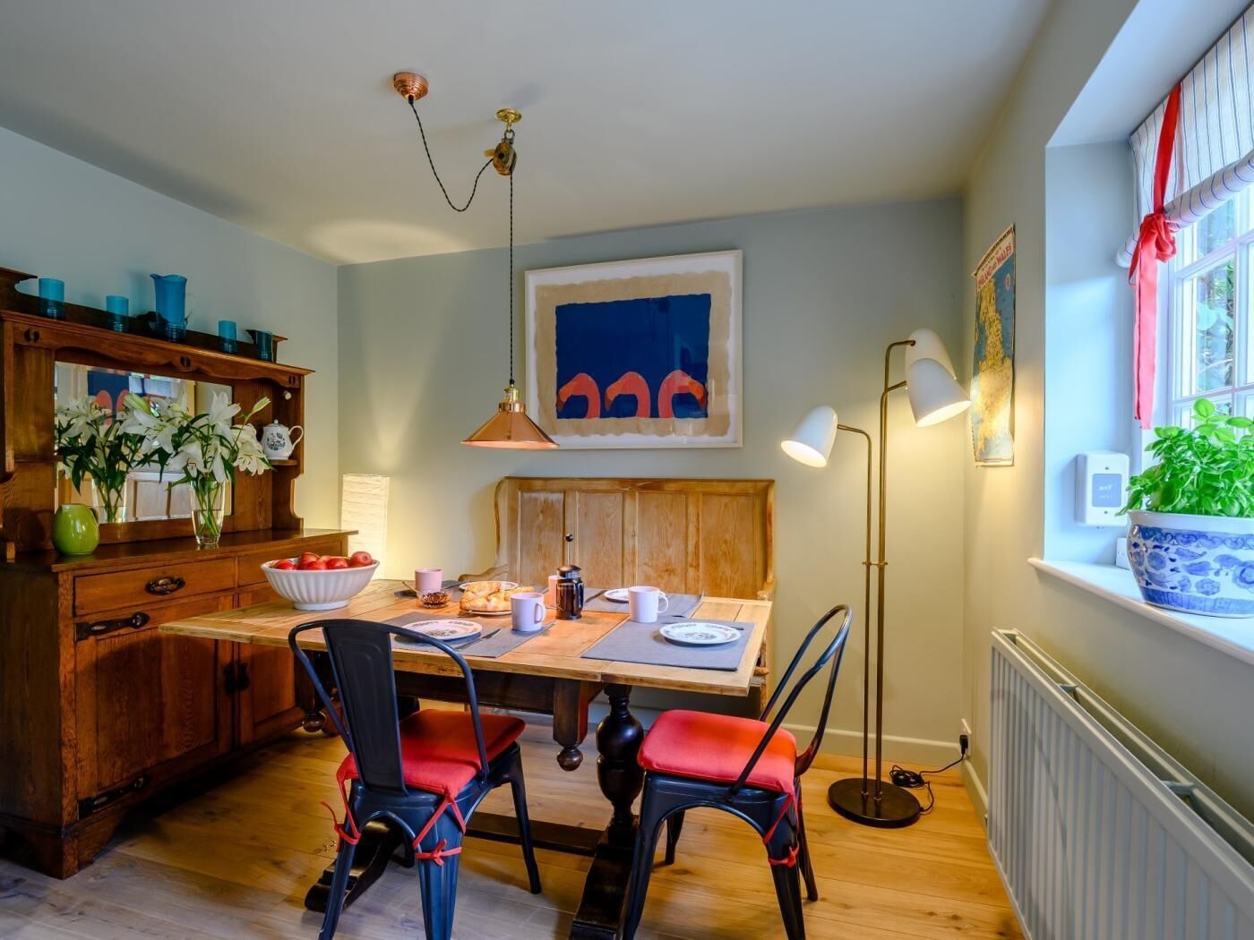 A dining area with a wooden table, chairs, a mirror, and a hanging light fixture.