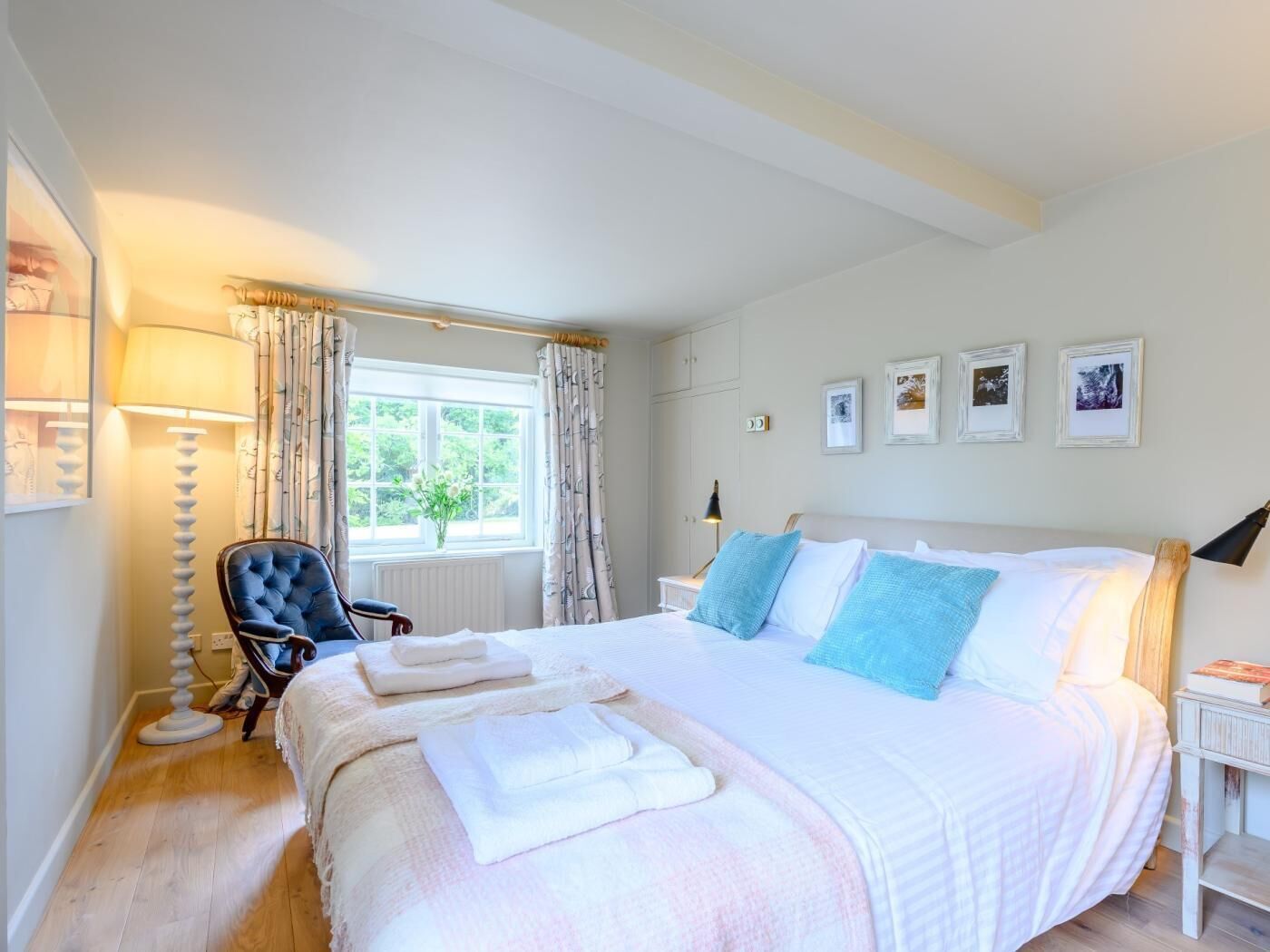A bedroom with a large bed, a chair, a window with curtains, and framed pictures on the wall.