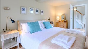 Ein Schlafzimmer mit einem Bett, Nachttischen, einer Kommode, einer Lampe, gerahmten Bildern an der Wand und einer Treppe.