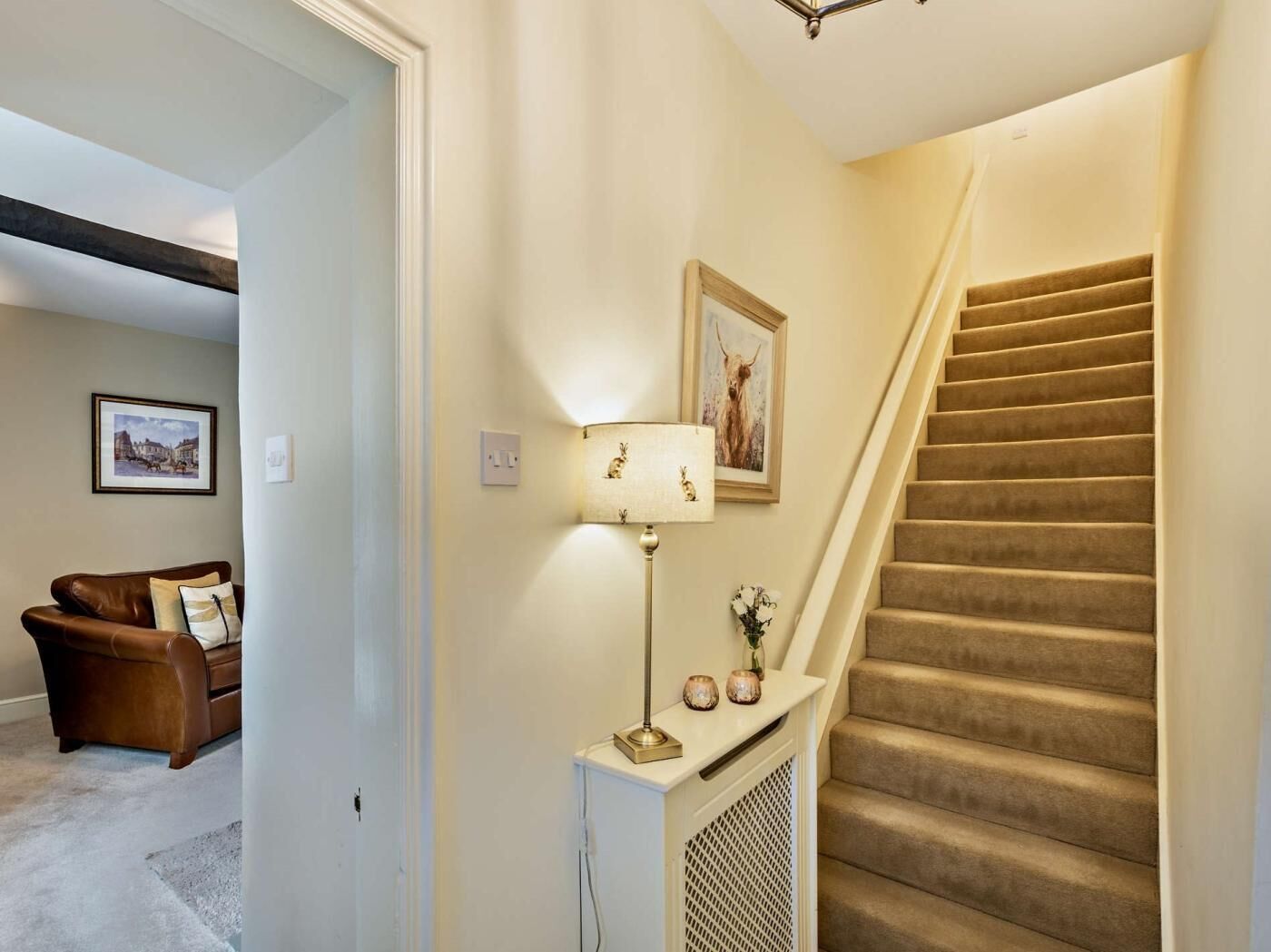 Un escalier avec des marches recouvertes de moquette, une lampe fixée au mur et un tableau encadré au-dessus.