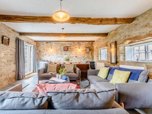 A cozy living room with stone walls, wooden beams, and a fireplace. There are two sofas, a coffee table, and a dining area with a table and chairs. - 4 Bed in Cardigan (oc-79046) (Ponthirwaun)