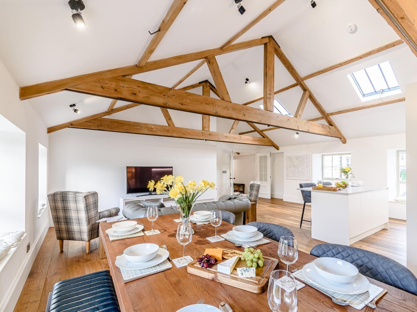 A spacious dining area with a wooden ceiling, a television, and a kitchen in the background.