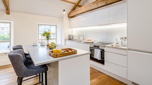 Et moderne køkken med hvide skabe, en central ø og et spiseområde med stole.