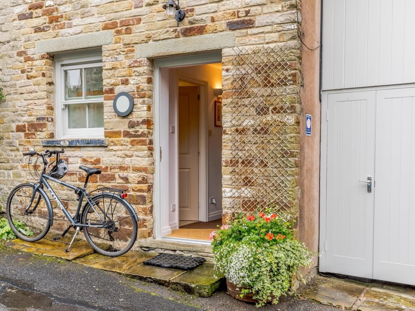 A stone building with a bicycle parked outside, a door leading to a room, and a flower pot on the ground.
