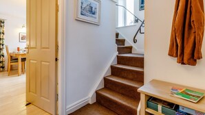 Een trap met beklede treden, een houten deur en een wandkapstok met een jas.