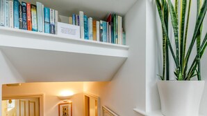 Een boekenplank met verschillende boeken, een potplant en een lijst met foto op de muur.