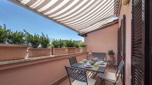 Une terrasse extérieure avec une table dressée pour le repas, entourée de chaises, et une marquise à rayures au-dessus.