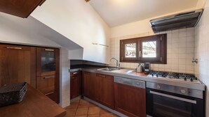 Une cuisine avec des meubles en bois, un lave-vaisselle, une cuisinière et une fenêtre donnant sur des immeubles.