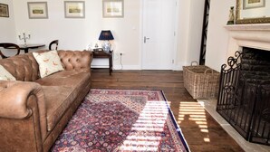 Ein Wohnzimmer mit braunem Ledersofa, einem gemusterten Teppich, einem Kamin und gerahmten Bildern an der Wand.