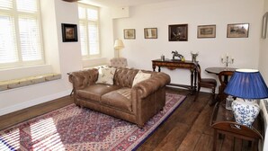 Ein Wohnzimmer mit braunem Ledersofa, einem gemusterten Teppich, einem Holztisch und einer blauen Lampe.