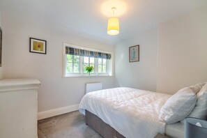 Ein Schlafzimmer mit einem Bett, einem Heizkörper, einem Fenster mit Vorhängen und einer Wandleuchte.