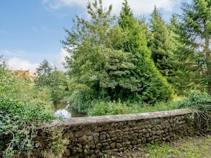 Eine steine Mauer neben einem Fluss, umgeben von dichtem Grün und Bäumen.