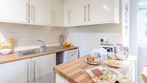 A modern kitchen with white cabinets, a wooden countertop, a sink, and a dining area with a table set for breakfast. - 3 Bed in Richmond (oc-79275) (Kiplin)