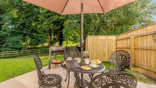 A patio with a table set for tea, surrounded by metal chairs, under a large umbrella. - 3 Bed in Richmond (oc-79275) (Kiplin)