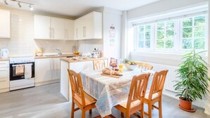 A bright kitchen with white cabinets, a dining table with chairs, a potted plant, and a window with a view of greenery. - 3 Bed in Richmond (oc-79275) (Kiplin)