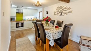 A dining area with a table set for four, surrounded by chairs, a chandelier, and a decorative tree wall piece. - 2 Bed in Driffield (oc-79280) (Wold Newton)